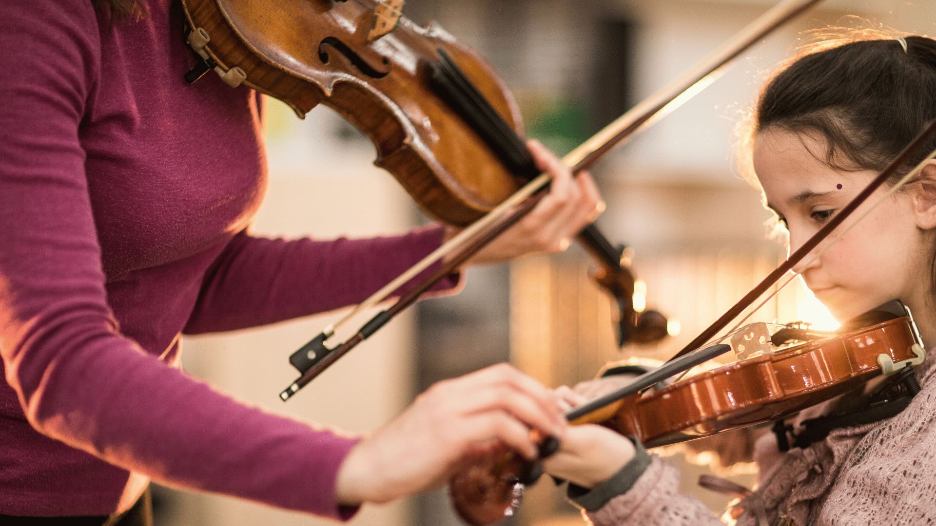 A teacher guiding a young student's bow arm